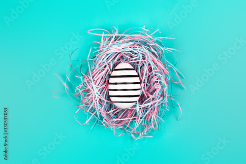 Graphic hand-painted in line egg in decorative nest on blue pastel background. Easter concept.