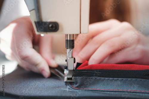 Hands of a seamstress doing precise work, close-up view. Needlewoman at overlock sewing machine doing professional work, concept of labor photo