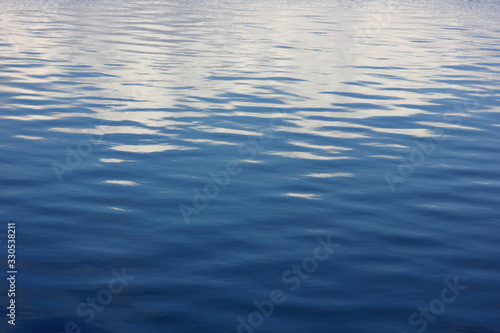 a soothing background with blue water of the river with small ripples and the reflected clouds