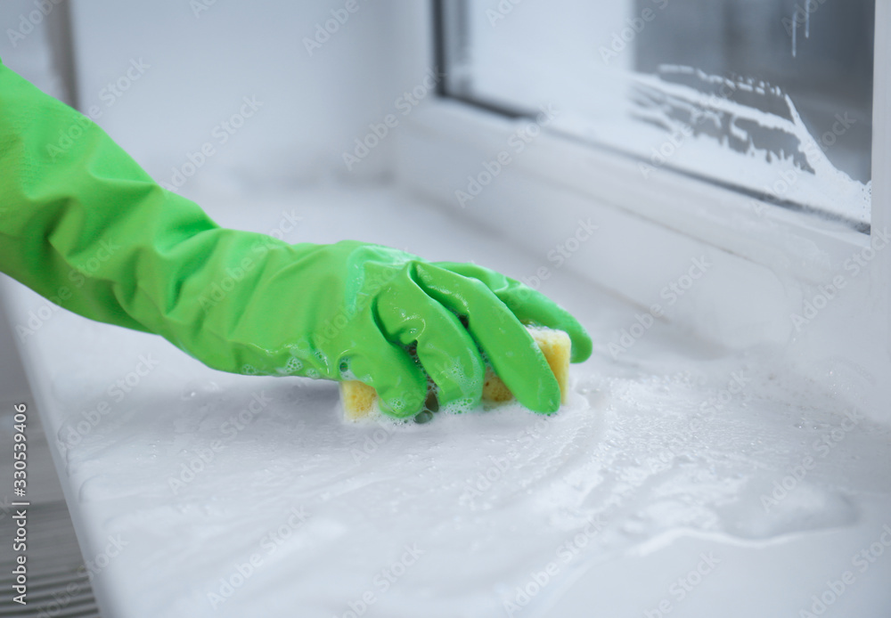 Woman cleaning window sill with sponge indoors, closeup