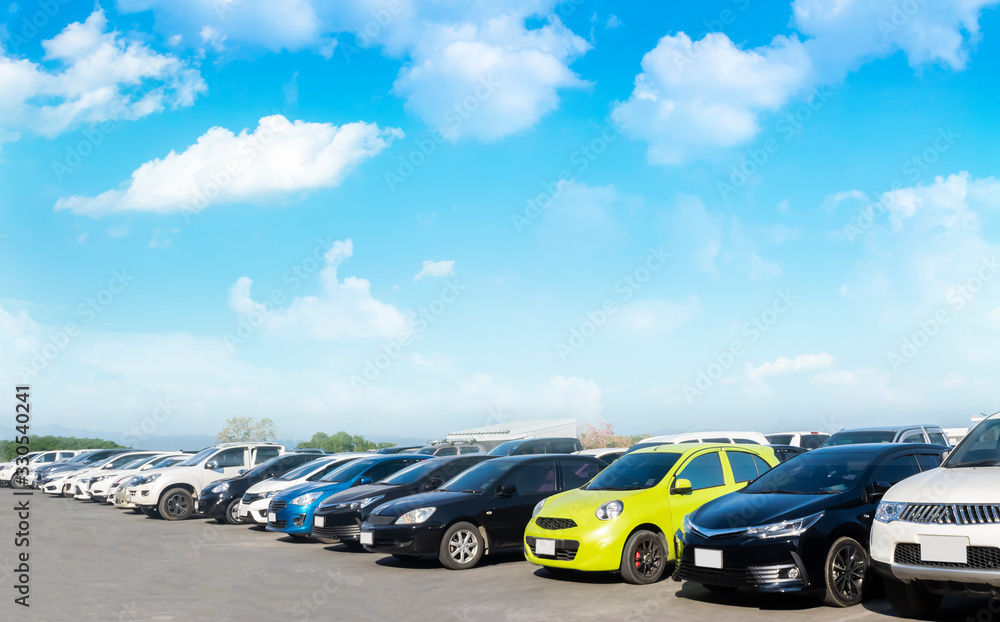 Car parked in large asphalt parking lot with white cloud and blue sky background.