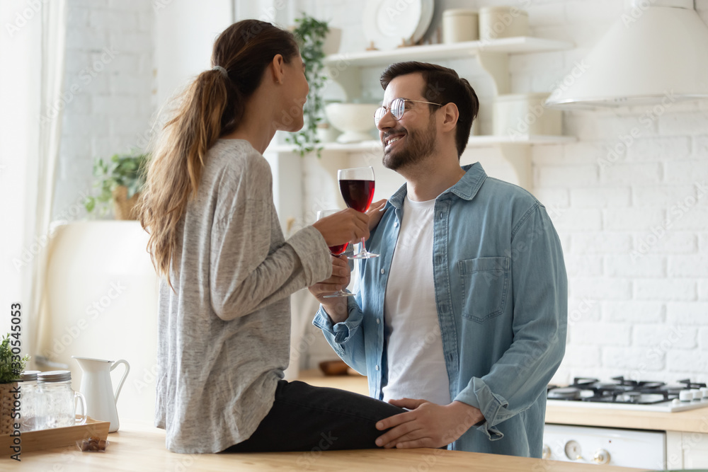 Beautiful woman sitting on wooden countertop in modern kitchen, enjoying tender moment with husband, happy girlfriend and boyfriend holding red wine glasses, romantic date, celebrating anniversary Beautiful woman sitting on wooden countertop in modern kitchen, enjoying tender moment with husband, happy girlfriend and boyfriend holding red wine glasses, romantic date, celebrating anniversary