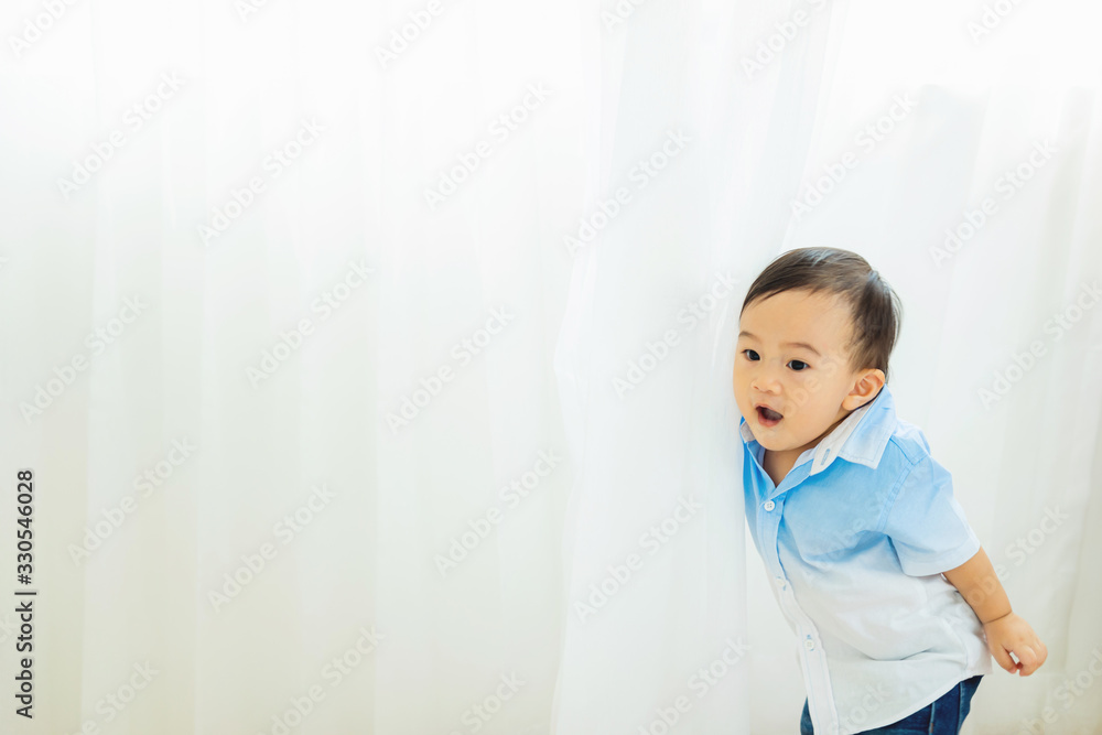 Cute little happy baby playing hide and seek in white curtain with free text copy space. Cute little happy baby playing hide and seek in white curtain with free text copy space.
