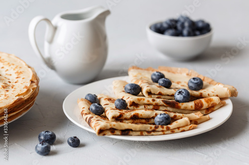 Thin pancakes on white plate with blueberries and sour cream. Grey background. Close up.