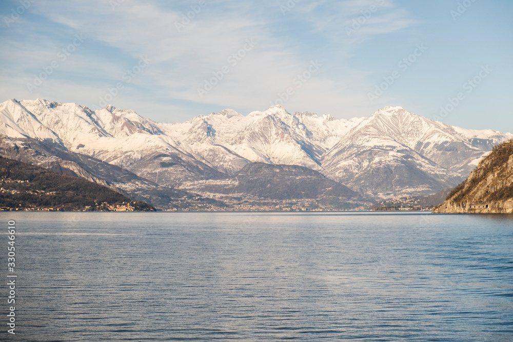 Panoramic of snowy mountain reflected in Lago di Como, Italy. Clouds and sunny sky. Scenic landscape Panoramic of snowy mountain reflected in Lago di Como, Italy. Clouds and sunny sky. Scenic landscape