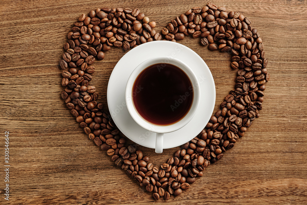 Composition with a cup of coffee in the center of a heart-shaped coffee bean Composition with a cup of coffee in the center of a heart-shaped coffee bean