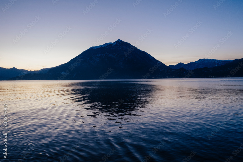 bluish mountain silhouette backlighting in a sunset with reflection in the lake