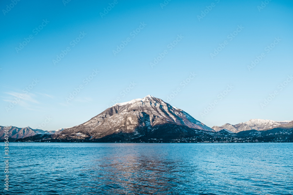 Panoramic of small snowy mountain reflected in Lago di Como in Italy, clear and sunny sky