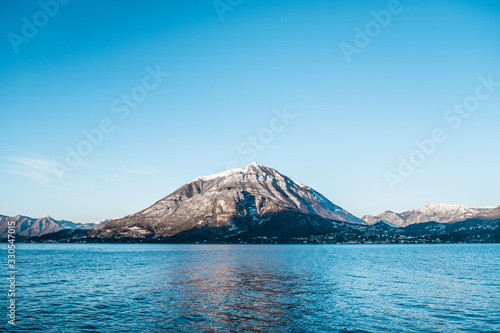 Panoramic of small snowy mountain reflected in Lago di Como in Italy, clear and sunny sky