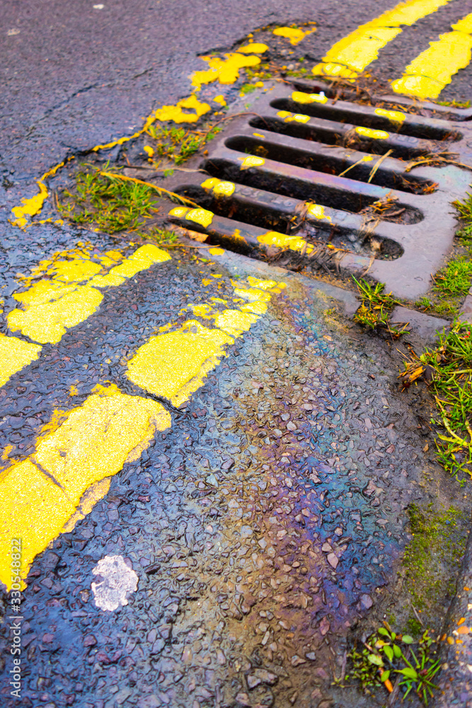 Obraz premium Petrol Gasoline Oil Spill on The Road Tarmac Rainbow Colour Pollution Running Down a Drain