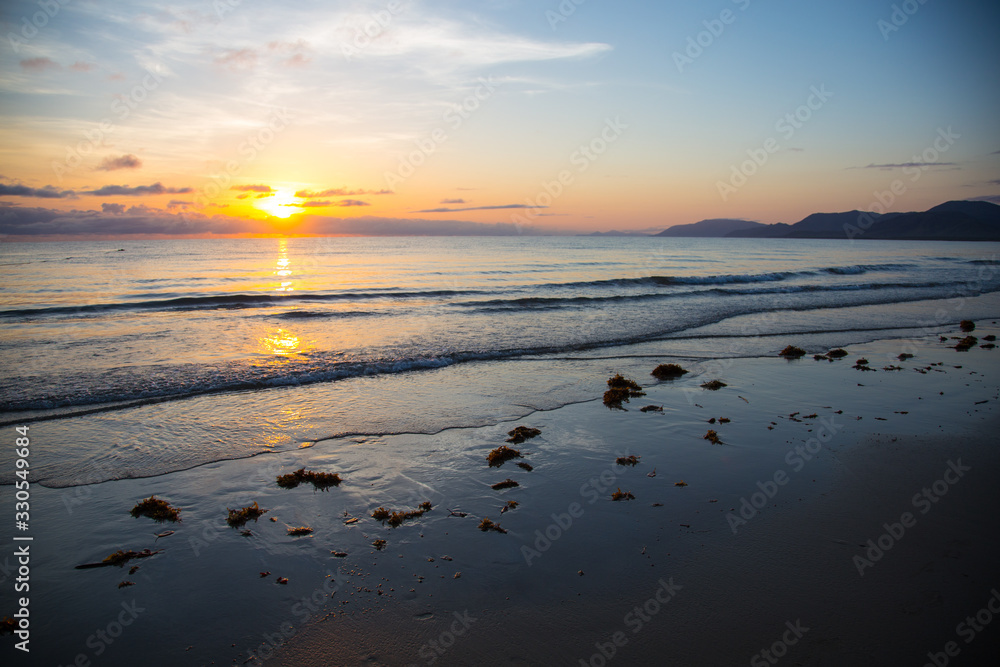 Sunrise at Four Mile Beach, Port Douglas, Queensland, Australia. Waves are breaking calm onto the beach and the colorful sunrise is reflected in the water.