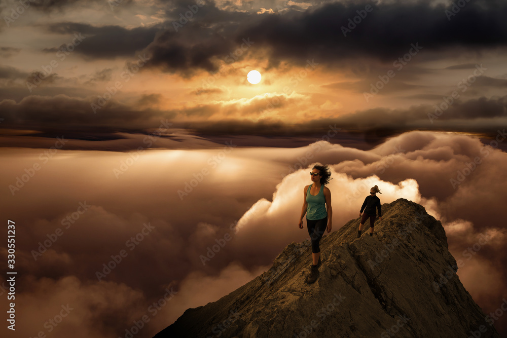 Girl Hiking on a Rocky Mountain Peak with Beautiful and striking view of the puffy clouds during vibrant sunset or sunrise. Nature Background. Concept: Freedom, Lifestyle, Adventure, Hike