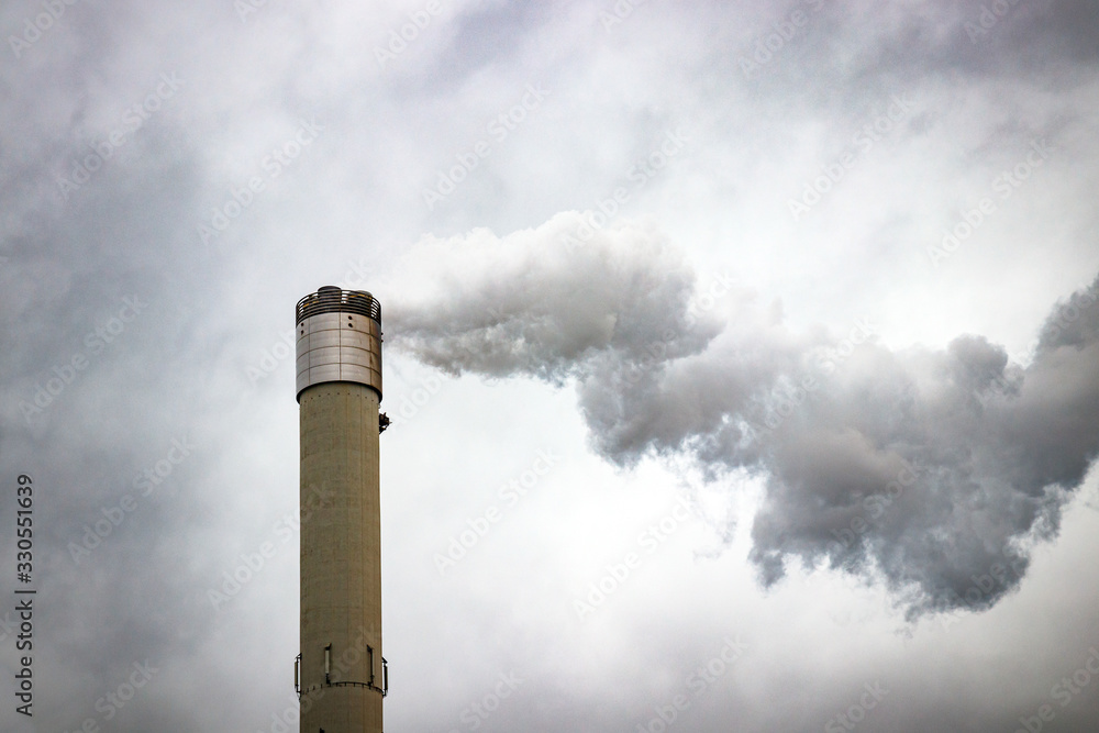 Tall chimney emitting gases into the atmosphere, causing air pollution. Gray, dramatic cloudy sky. Tall chimney emitting gases into the atmosphere, causing air pollution. Gray, dramatic cloudy sky.