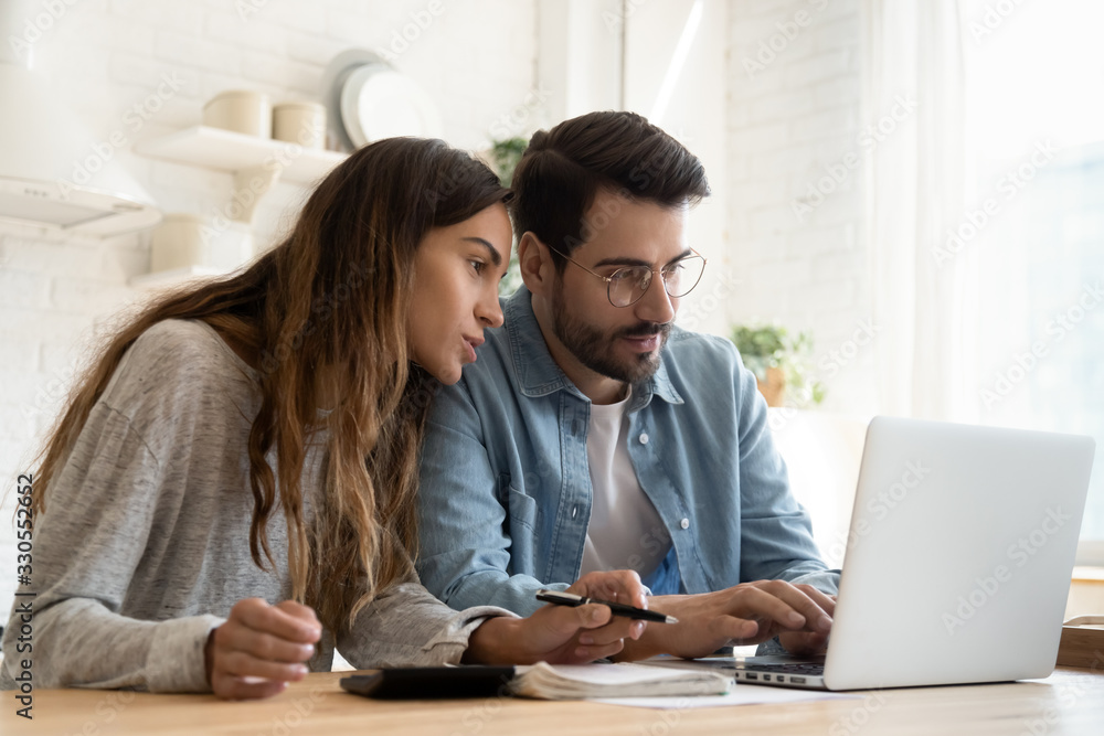 Focused young couple calculating bills, discussing planning budget  together, serious wife and husband looking at laptop screen, using online  banking services and calculator, checking finances Stock Photo | Adobe Stock