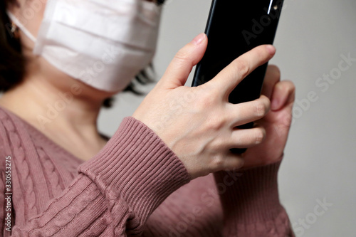 Woman in white medical mask using smartphone, close-up mobile phone in female hands. Concept of illness, search for coronavirus symptoms, protection from the COVID-19 epidemic