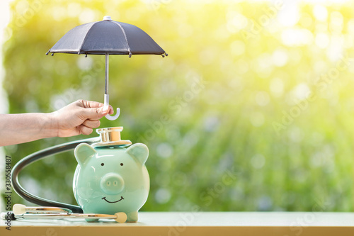 Piggy bank use stethoscope check hygiene and woman hand hold the black umbrella for protect on sunlight in the public park, to prevent for money and loans to planned investment in the future concept.