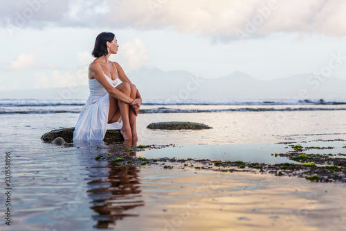 Beautiful woman by the ocean at sunset