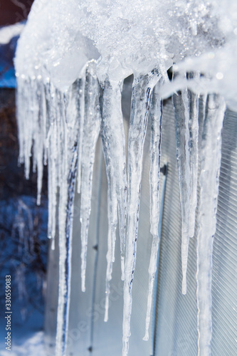 The icicles are melting. Spring thaw. Warm winter . Icicles close up. Close up of a large wavy icicle with more melting icicles beside it and a soft winter background.