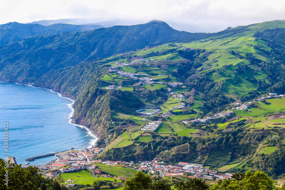 Scenic lookout with coastal village surrounded by cloud covered mountains, ocean, and lush green landscape