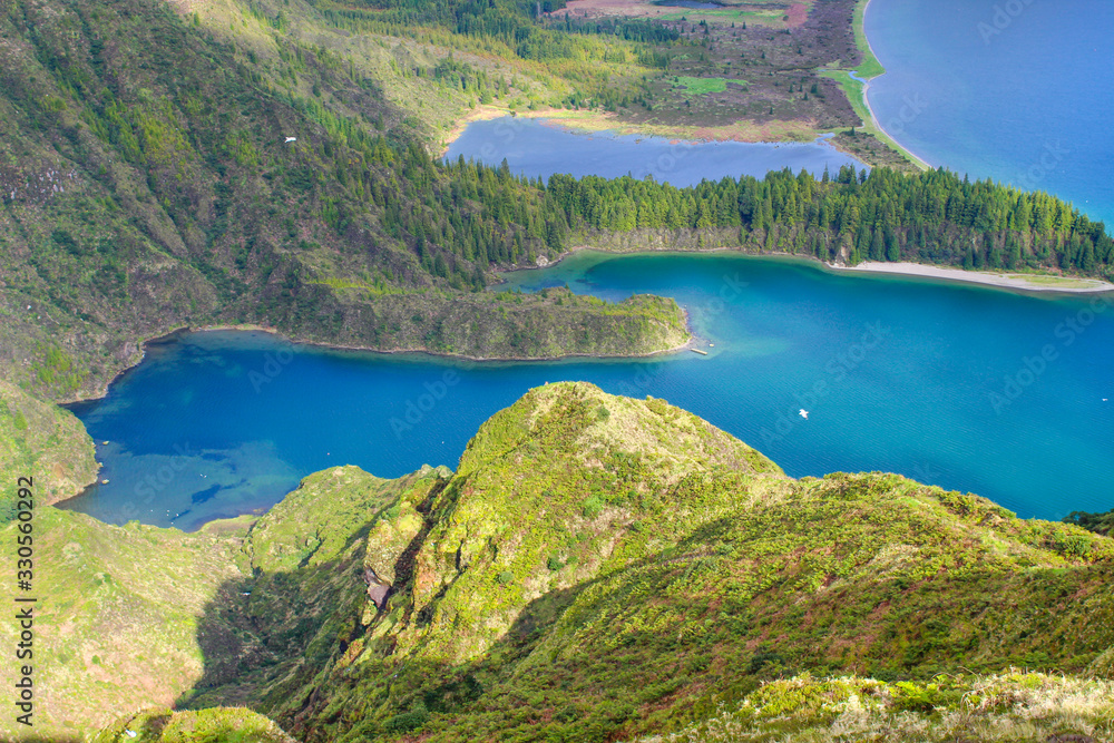 Blue lagoon in volcanic crater lake on a sunny day surrounded by lush green mountains