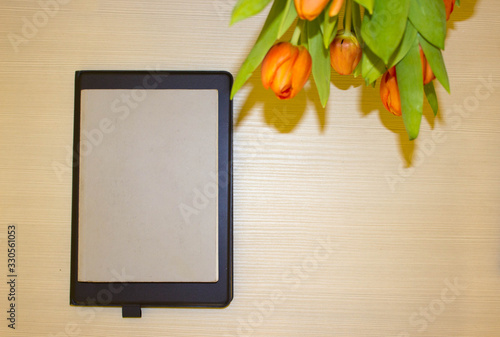 Smart working place: smarpad, orange tulips, notepad on wooden background. Free copy space