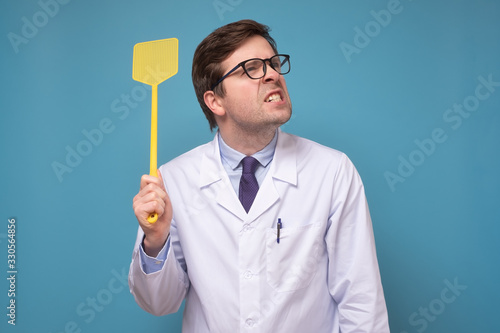 Slika na platnu Young caucasian medical man doctor holding a fly swatter looking for insect or v