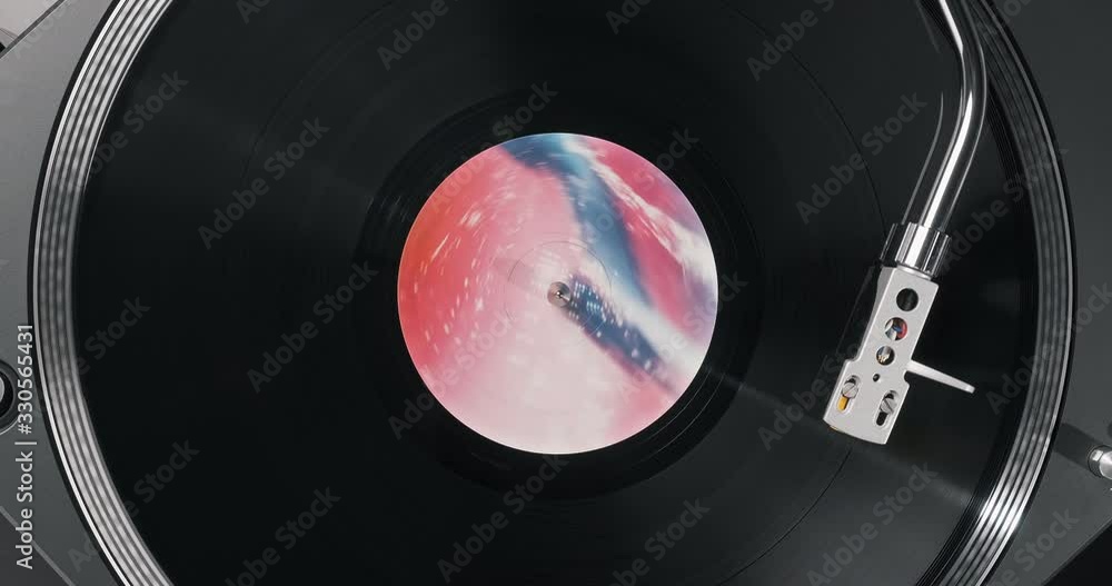 Black vinyl record on DJ player. Black vinyl background pink and blue label in center. Rotating plate close-up on turntable. Needle stylus. Macro Top view. Popular styles of disco from 90s, 70s, 80s