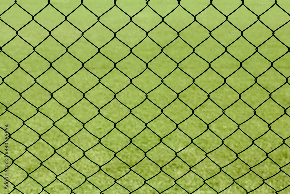 Fototapeta premium Green mesh fence against the backdrop of a sports field