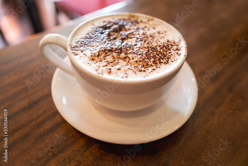 Cappuccino in a white cup and saucer on a wooden table. Shallow focus.