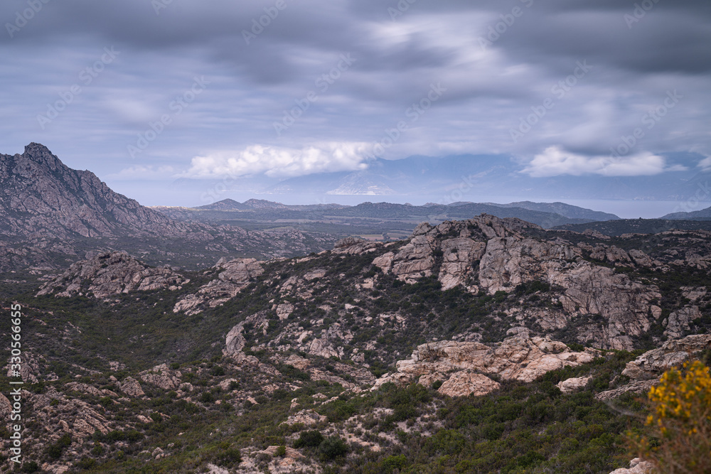Desert des Agriates - rugged scenary, garrigue vegetation. Mediterranean Sea in the distance and an outline of Cap Corse