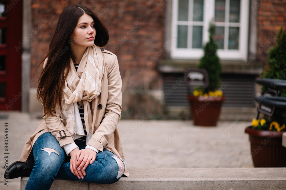 Fototapeta premium Street fashion concept. Vintage portrait of young woman in spring coat and hat. Flattering hair.