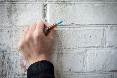 Filled syringe in human hands on a background of a white brick wall. Addiction concept.