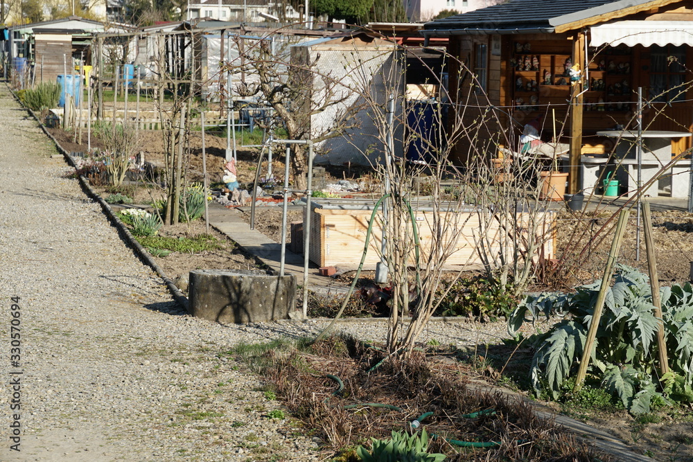 A gravel path in allotment garden colony and small garden houses on a sunny day in spring in village Urdorf in Switzerland. A gravel path in allotment garden colony and small garden houses on a sunny day in spring in village Urdorf in Switzerland.