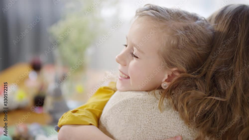Handheld shot of happy girl smiling and hugging her unrecognizable mother. Tray with Easter eggs and bunny figurine standing on table Handheld shot of happy girl smiling and hugging her unrecognizable mother. Tray with Easter eggs and bunny figurine standing on table