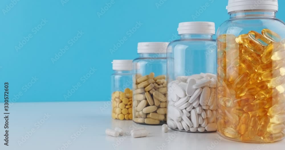 Bottles transparent pills orange capsules blue background. Woman's hand pours gel capsules bottle white surface. Nutritional Supplements, Vitamins. Omega 3, multivitamins, Calcium, antibiotics. Health Bottles transparent pills orange capsules blue background. Woman's hand pours gel capsules bottle white surface. Nutritional Supplements, Vitamins. Omega 3, multivitamins, Calcium, antibiotics. Health
