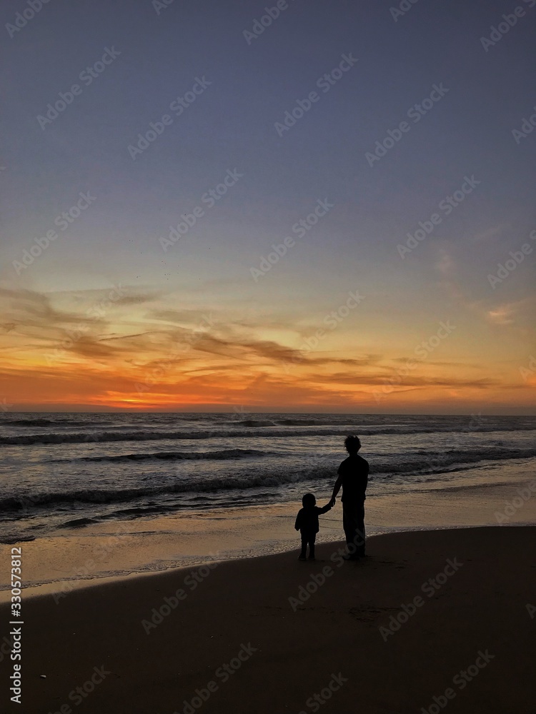 silhouette of man and a kid on the beach at sunset