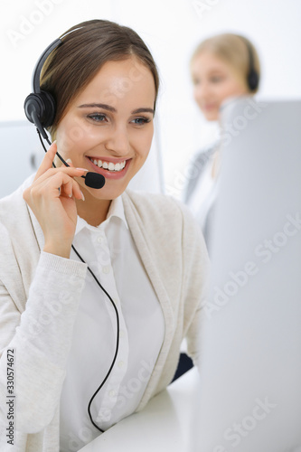 Call center. Group of operators at work. Focus on beautiful woman receptionist in headset at customer service white colored office. Business concept