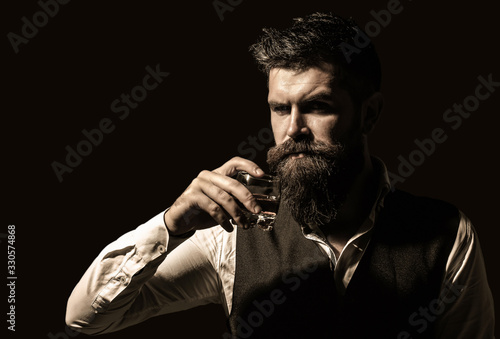 Man holding a glass of whisky. Sipping whiskey. Man with beard holds glass brandy. Macho drinking. Degustation, tasting. Bearded drink cognac. Sommelier tastes drink. Portrait of man with thick beard.