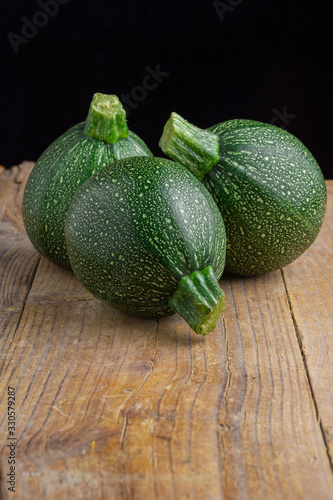 Top view of three round zucchini on rustic wooden board and black background in vertical