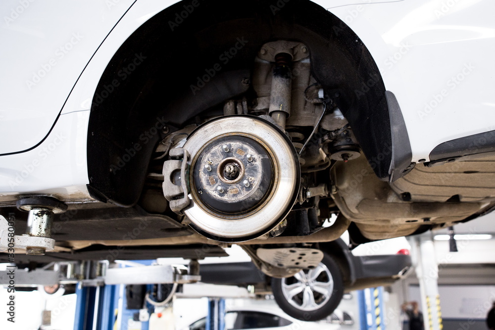 Car raised on the car lift. Brake disc with brake pads. A car with its wheels removed at a service station. Car raised on the car lift. Brake disc with brake pads. A car with its wheels removed at a service station.
