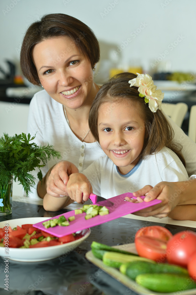 Cute little girl with her mother cooking together at kitchen table