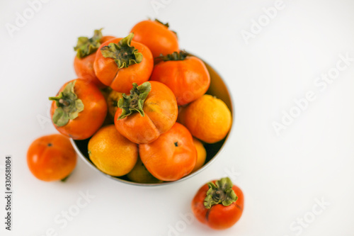 Persimmon closeup lying in a bowl on a white background. Organic farming, healthy food concept, eco-friendly products, vegetarian, raw products.