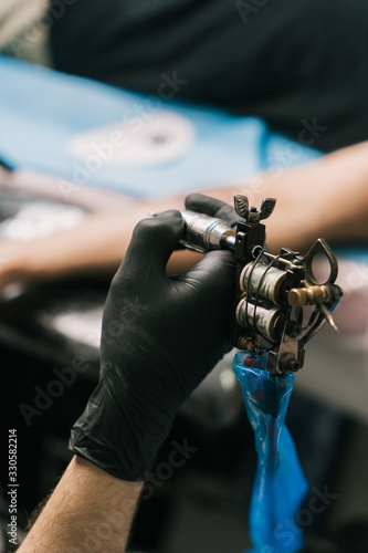 A selective focus shot of the hand of a tattoo artist wearing a black glove and holding a tattoo gun