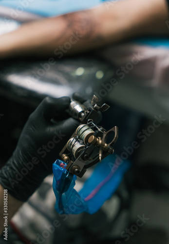 A selective focus shot of a hand of a tattoo artist wearing a black glove and holding a tattoogun