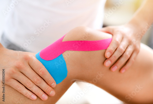 Photos Kinesiology taping treatment with blue and pink tape on athlete patient injured knee