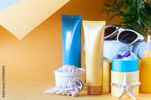 Suncare bottles, glasses, starfish palm leaves on a yellow background. Beauty and care in the summer. Copy space
