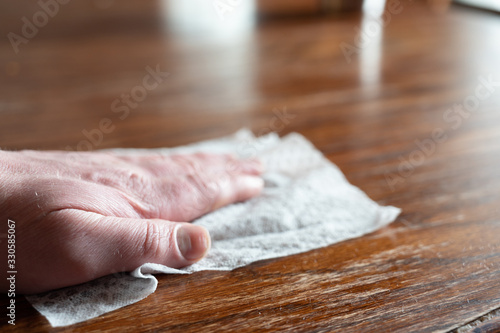 Hand holding sanitizing wipe to disinfect a wooden table top