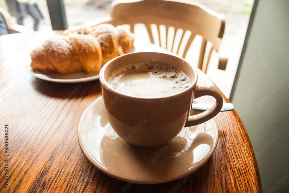 Food and drink concept. Cup of fresh coffee with foam on a wooden table with a croissant. Delicious French breakfast. Tasty food. Food and drink concept. Cup of fresh coffee with foam on a wooden table with a croissant. Delicious French breakfast. Tasty food.