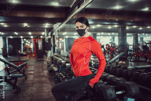 Coronavirus covid-19 prevention, fitness girl with a medical mask posing in gym. Fighting viruses.