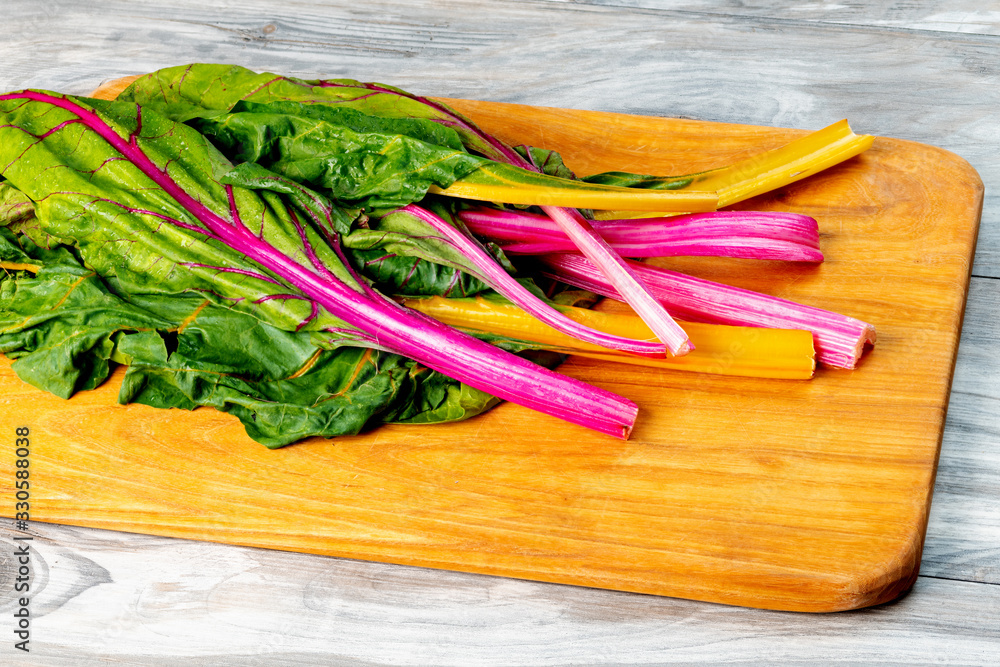 Leafy vegetables on a wooden cutting board with colorful stems